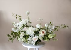 a white flower arrangement sitting on top of a small table next to a pink wall