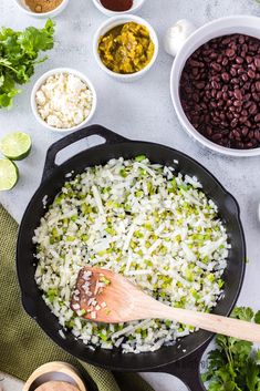 rice and beans are being cooked in a skillet with wooden spoons on the side