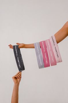 two hands are holding different colored wristbands with the same message on each arm