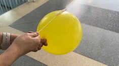 a person holding a yellow balloon with string attached to it's end in an airport