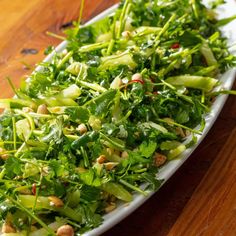 a plate filled with greens and nuts on top of a wooden table