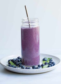 a blueberry smoothie in a mason jar on a white plate with fresh blueberries