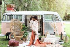 two women standing in front of a vw van with wicker chairs and rugs