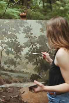 a woman holding a paintbrush in front of a painting