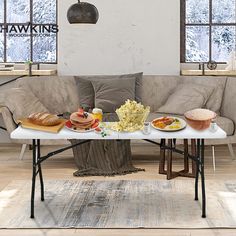 a coffee table with food on it in front of a couch and two large windows