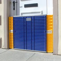 a blue and yellow door is open on the side of a white building with an orange gate