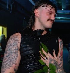 a man with long hair and tattoos on his arm holding a green leafy plant