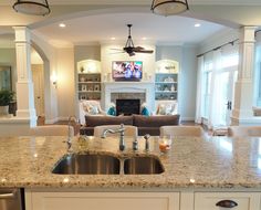 a kitchen island with two sinks in front of a fire place and couches behind it