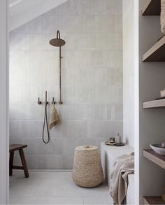 a white tiled bathroom with a wooden stool and shower head on the wall next to it