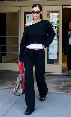 a woman in black is standing on the sidewalk with her hands in her pockets and wearing sunglasses