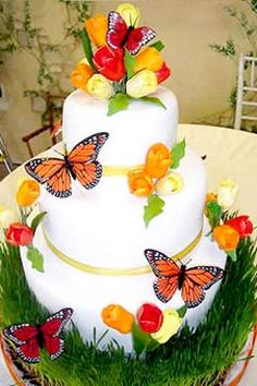 a three tiered cake with butterflies on the top and grass around it, sitting on a table