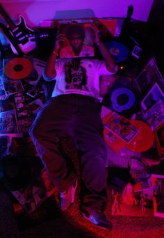 a man laying on the floor in front of a wall covered with musical instruments and cds