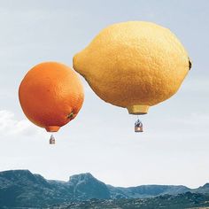 two lemons and an orange flying in the air with mountains in the back ground