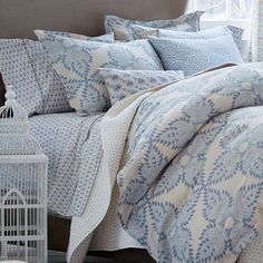 a bed covered in blue and white comforter next to a window with birdcage