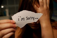 a woman holding up a piece of paper with the words i'm sorry written on it