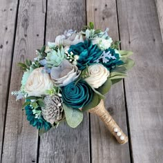 a bridal bouquet with blue flowers and greenery on a wooden floor in front of wood planks