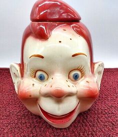 an old clown mask with red hair and blue eyes on a pink carpeted floor