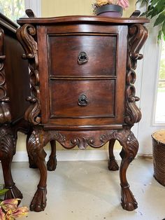 an ornate wooden cabinet with drawers in a room next to a potted plant on the floor