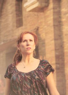 a woman standing in front of a brick building with her hand on her hip and looking off into the distance