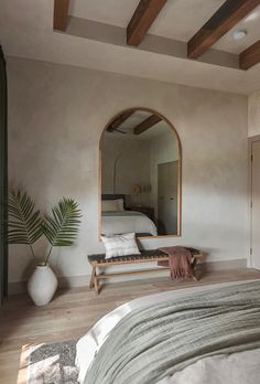 a bedroom with a bed, mirror and plant in it