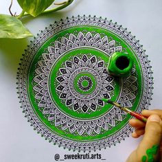 a person is painting a green and white circular design on paper with paintbrushes