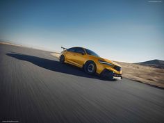 a yellow sports car driving on the road in the middle of an open desert area