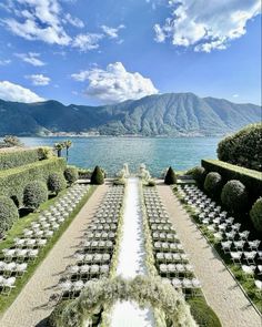 an outdoor ceremony set up with chairs and flowers on the lawn next to water in front of mountains