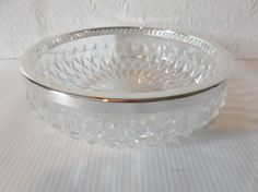 a clear glass bowl sitting on top of a white tableclothed surface with a silver rim