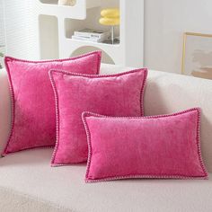 three pink pillows sitting on top of a white couch