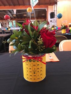 a red rose in a yellow tin with a black table cloth and name tag on it