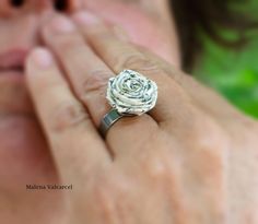 a close up of a person's hand with a ring on their finger and a flower in the middle