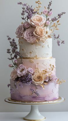 a three tiered cake with flowers on the top and bottom is decorated in white, purple and gold