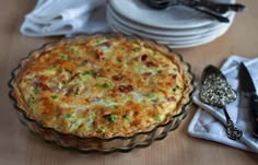 a quiche sitting on top of a wooden table next to plates and utensils