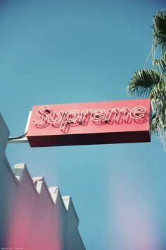 a pink sign that says supreme hanging from the side of a building in front of a palm tree