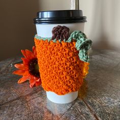 a coffee cup cozying with some crochet on the side and a sunflower