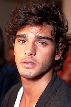 a close up of a person wearing a black jacket and white shirt with curly hair