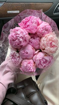 a bouquet of pink peonies sitting on top of a car seat next to a glove