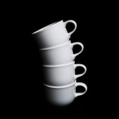 four white cups stacked on top of each other in the middle of a black background