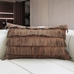 a brown fringe pillow sitting on top of a white couch