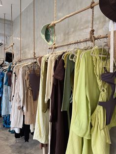 clothes hanging up in a clothing store with hats and umbrellas on the racks next to them