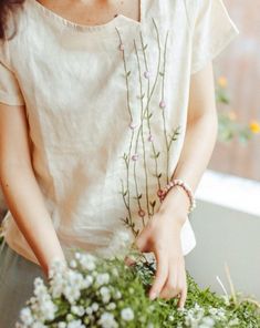 a woman arranging flowers in a vase with her hands on the top of the plant