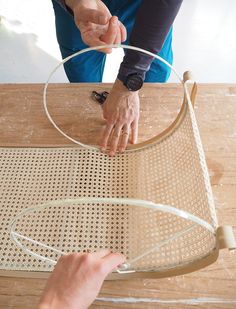 two hands are working on an object made out of wire and wood, while another hand is holding something in the other hand