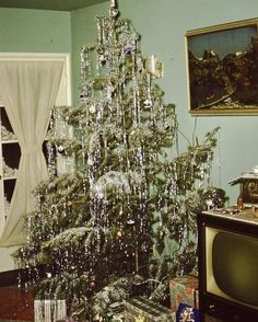 a small christmas tree in the corner of a room next to a tv and window