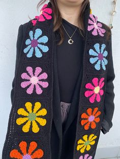 a woman standing in front of a white wall wearing a black jacket with multicolored flowers on it