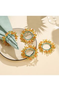 three pieces of jewelry sitting on top of a plate next to wine glasses and napkins