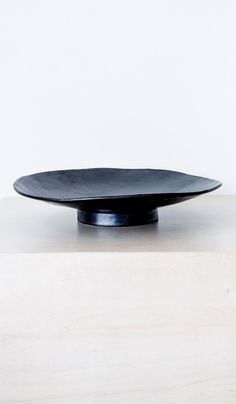 a black plate sitting on top of a wooden table next to a white wall in the background