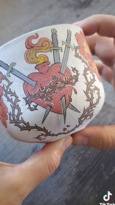 someone is holding an egg decorated with swords and flowers on it's side, while another hand holds the top