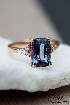 a fancy ring with a blue stone surrounded by white diamonds on a piece of rock