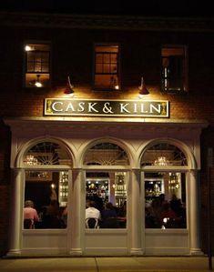 people are sitting at the front of a restaurant with lights on and windows lit up