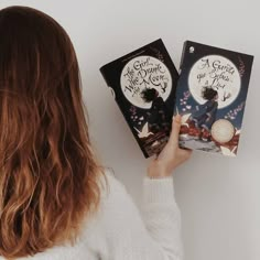 a woman is holding two books in her hands and looking at the book on the cover